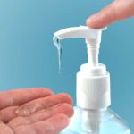 A finger pressing a pump dispensing clear hand sanitizer onto a palm.