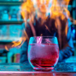 A flaming cocktail glass glowing with vibrant colors on a bar counter.